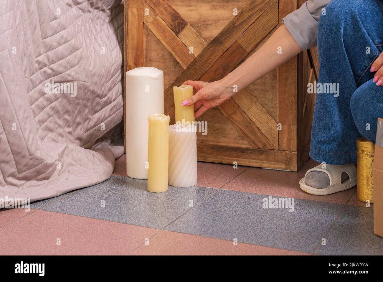 Das junge Designermädchen in Jeans stellt dekorative Kerzen neben Bett und Nachttisch. Vorbereitung der Wohnung für die Party. Stockfoto