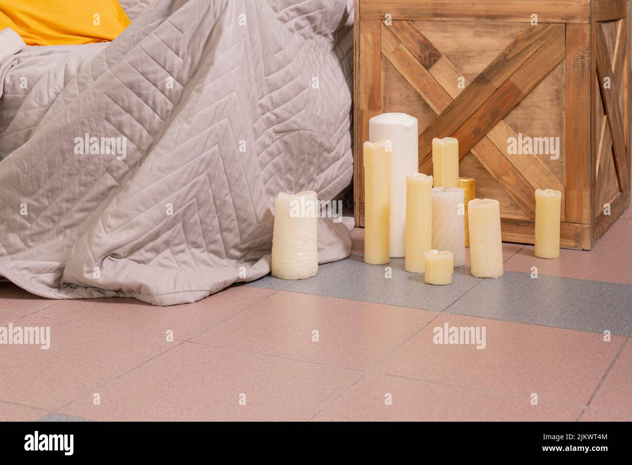 Kleine Gruppe von Kerzen in verschiedenen Formen, Größen und Farben steht auf dem Boden des Schlafzimmers neben dem Bett und dem Nachttisch. Stockfoto