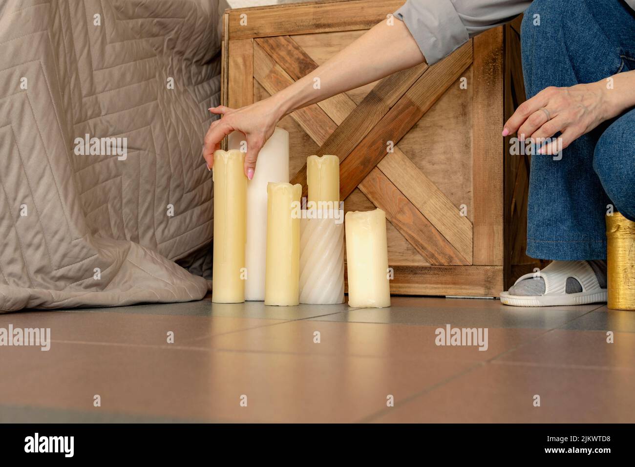 Das junge Designermädchen in Jeans stellt dekorative Kerzen neben Bett und Nachttisch. Vorbereitung der Wohnung für die Party. Stockfoto