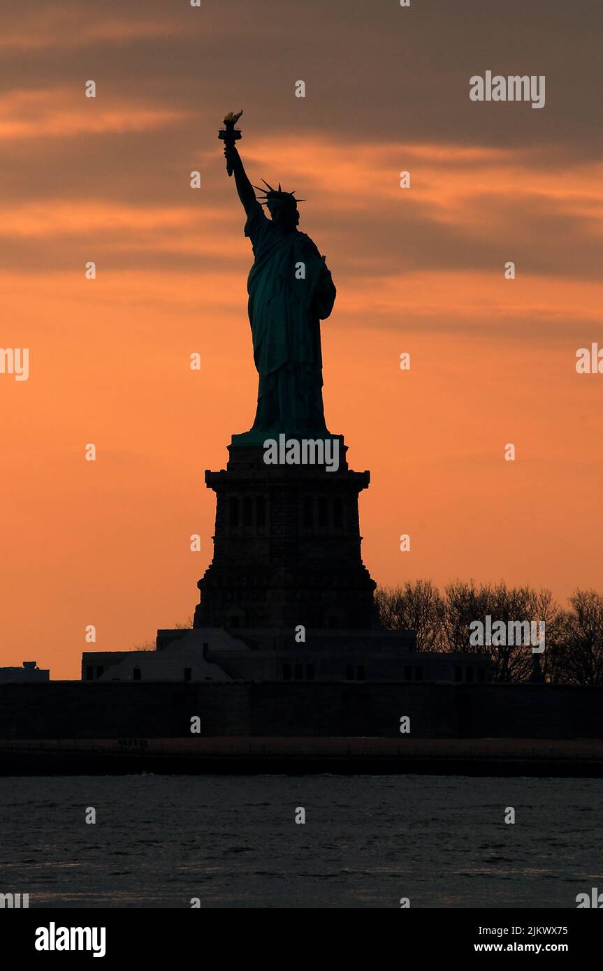 Silhouette der Freiheitsstatue gegen ein leuchtendes orangefarbenes Sonnenuntergangshimmel-Konzept für NYC-Wahrzeichen, amerikanischen Patriotismus und Symbol der Freiheit in Amerika Stockfoto