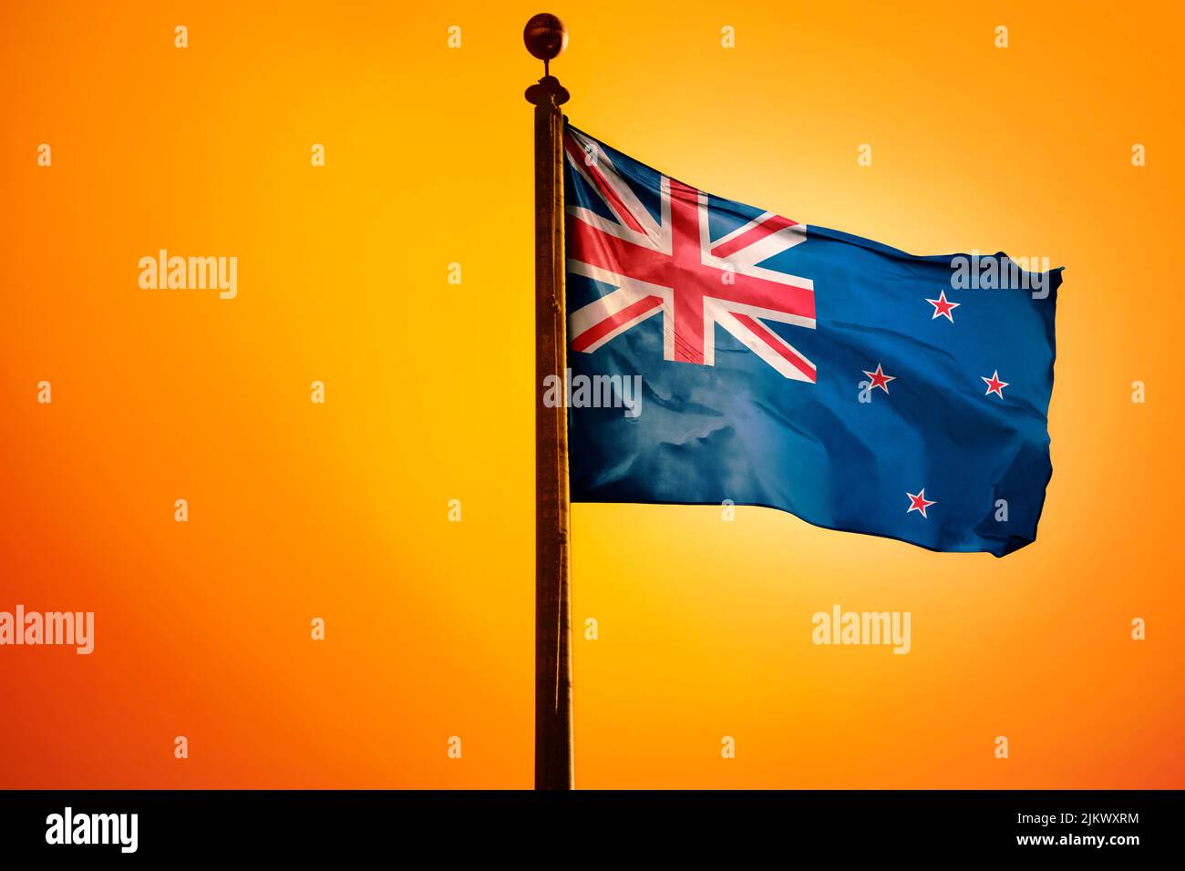 Die Nationalflagge Neuseelands auf einem Fahnenmast, isoliert auf einem orangen Hintergrund Stockfoto