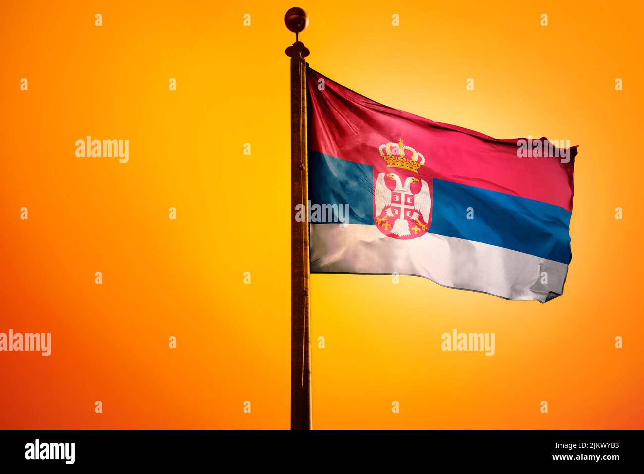 Die Nationalflagge Serbiens auf einem Fahnenmast, isoliert auf einem orangen Hintergrund Stockfoto