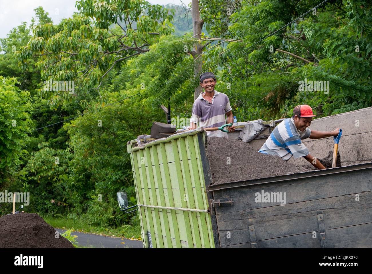 Ein paar lächelnde, glückliche balinesische Männer arbeiten und schaufeln Erde aus einem Lastwagen Stockfoto