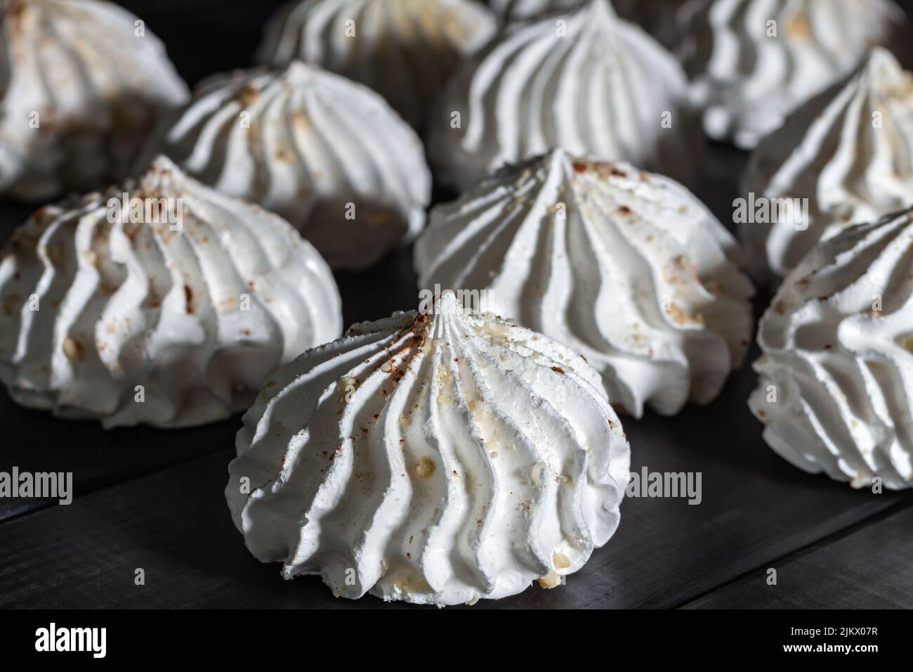 Nahaufnahme Meringues mit Nüssen auf dunklem Holztisch. Low-Key, Seitenansicht, selektiver Fokus. Dessert Hintergrund. Süßigkeiten. Essen. Weiße süße Meringu Stockfoto
