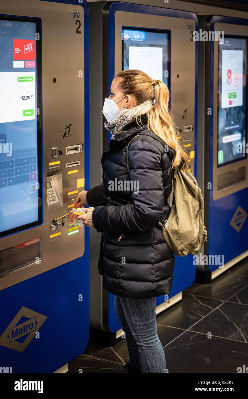 Junges Mädchen mit einer Maske beim Kauf des U-Bahn-Tickets in der Maschine, es ist Winter in der Madrid Metro Stockfoto