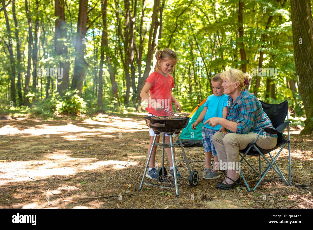Eine Nahaufnahme von Kindern mit ihrer Großmutter, die Spaß beim Grillen in einem Wald hat Stockfoto