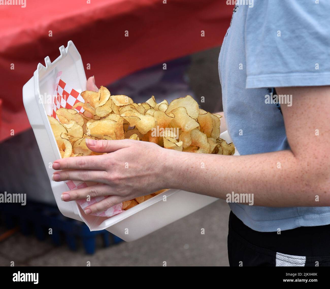 Ein junges Mädchen kauft bei einem Lebensmittelhändler auf einem Outdoor-Festival in Santa Fe, New Mexico, einen Karton mit Bandfrites. Stockfoto