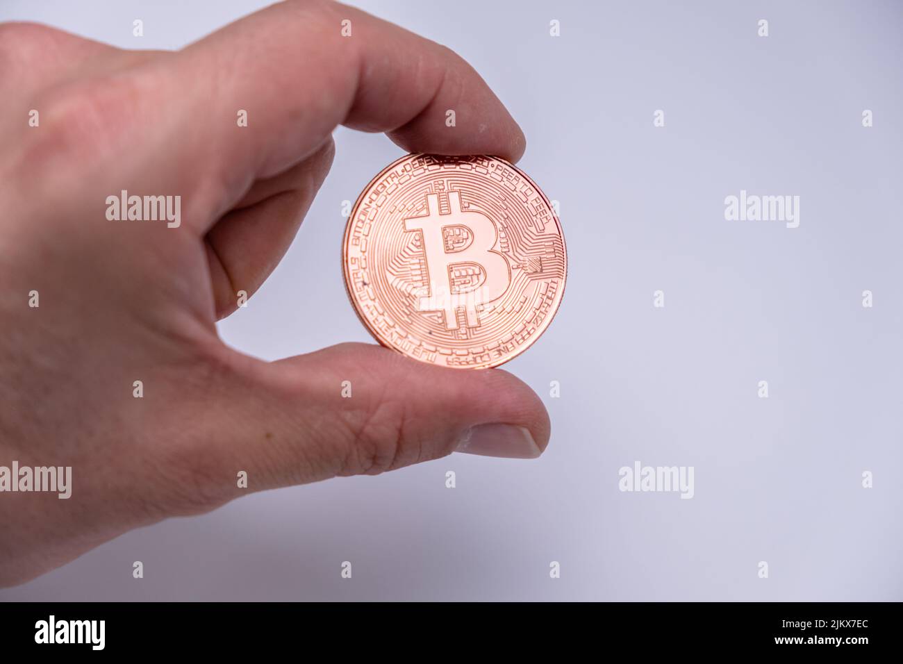 Männlicher Handfinger mit Bitcoin Kryptowährung Münze. Nahaufnahme einer Roségold-Bitmünze auf weißem Hintergrund. BTC beliebteste Krypto-Währung Mo Stockfoto