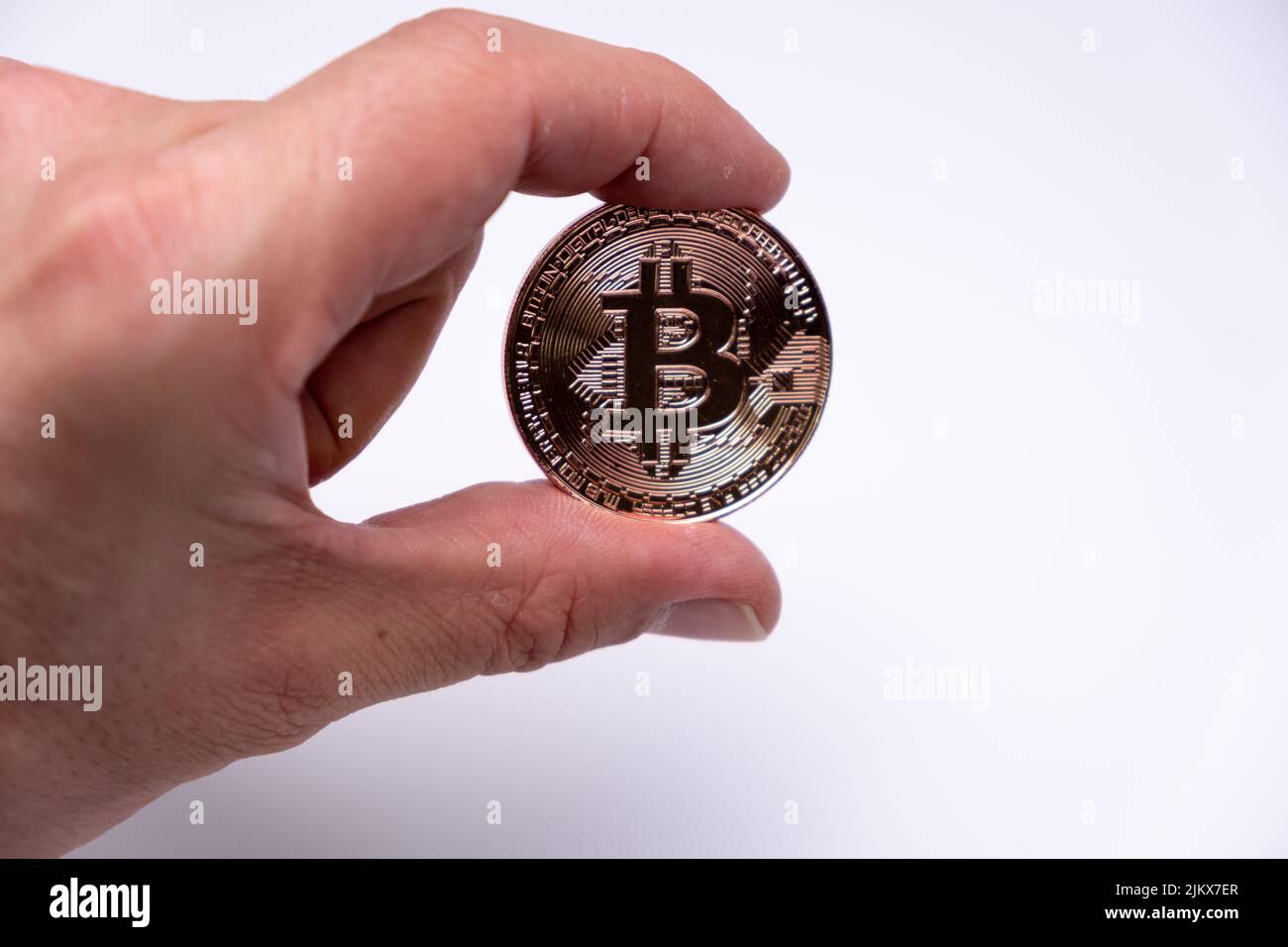 Männlicher Handfinger mit Bitcoin Kryptowährung Münze. Nahaufnahme einer Roségold-Bitmünze auf weißem Hintergrund. BTC beliebteste Krypto-Währung Mo Stockfoto