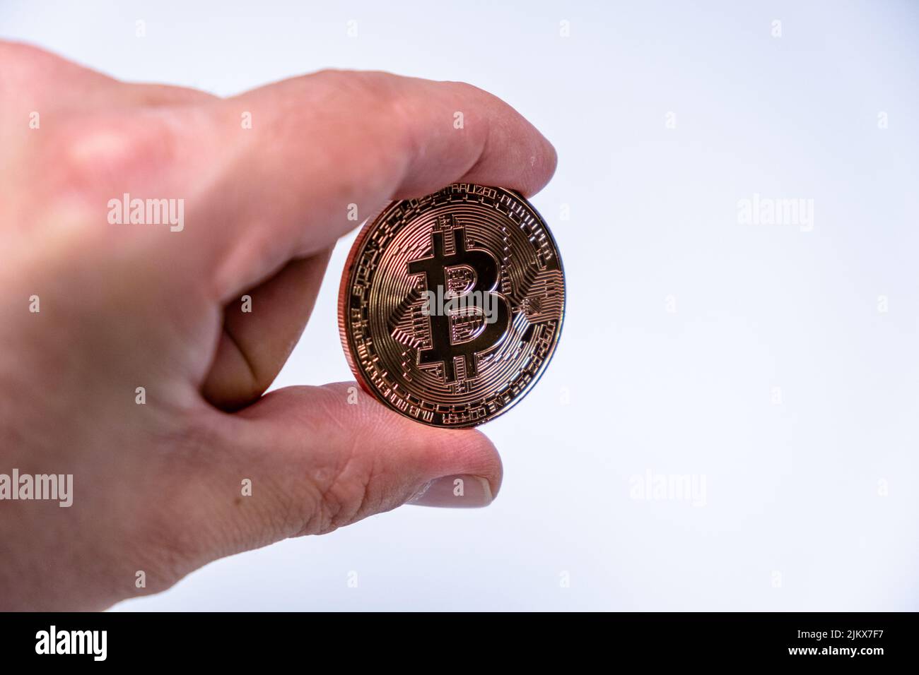 Männlicher Handfinger mit Bitcoin Kryptowährung Münze. Nahaufnahme einer Roségold-Bitmünze auf weißem Hintergrund. BTC beliebteste Krypto-Währung Mo Stockfoto