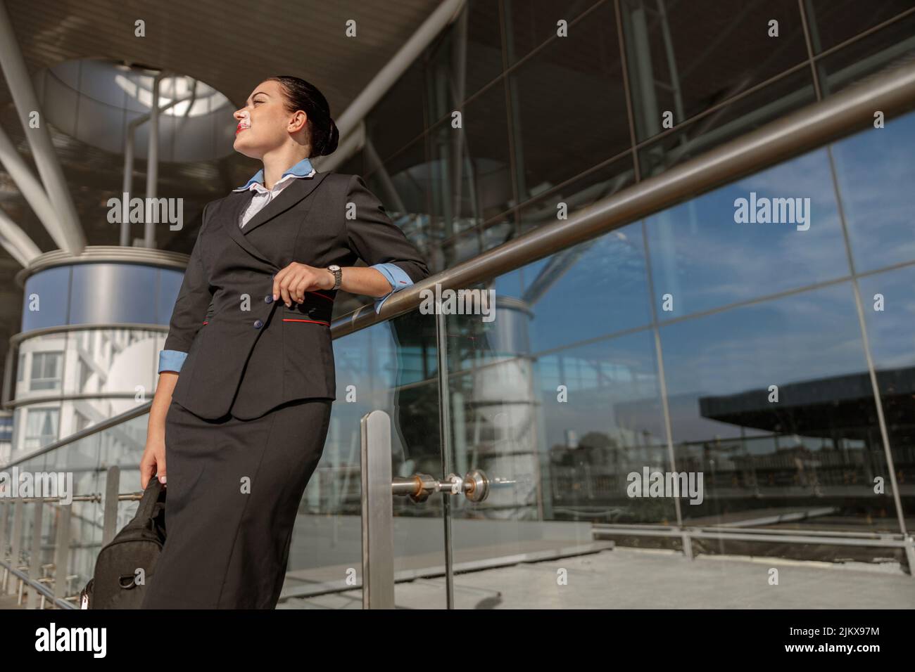 Attraktive Stewardess mit Tasche, die auf einem Metallgestell aufliegt und nach draußen schaut Stockfoto