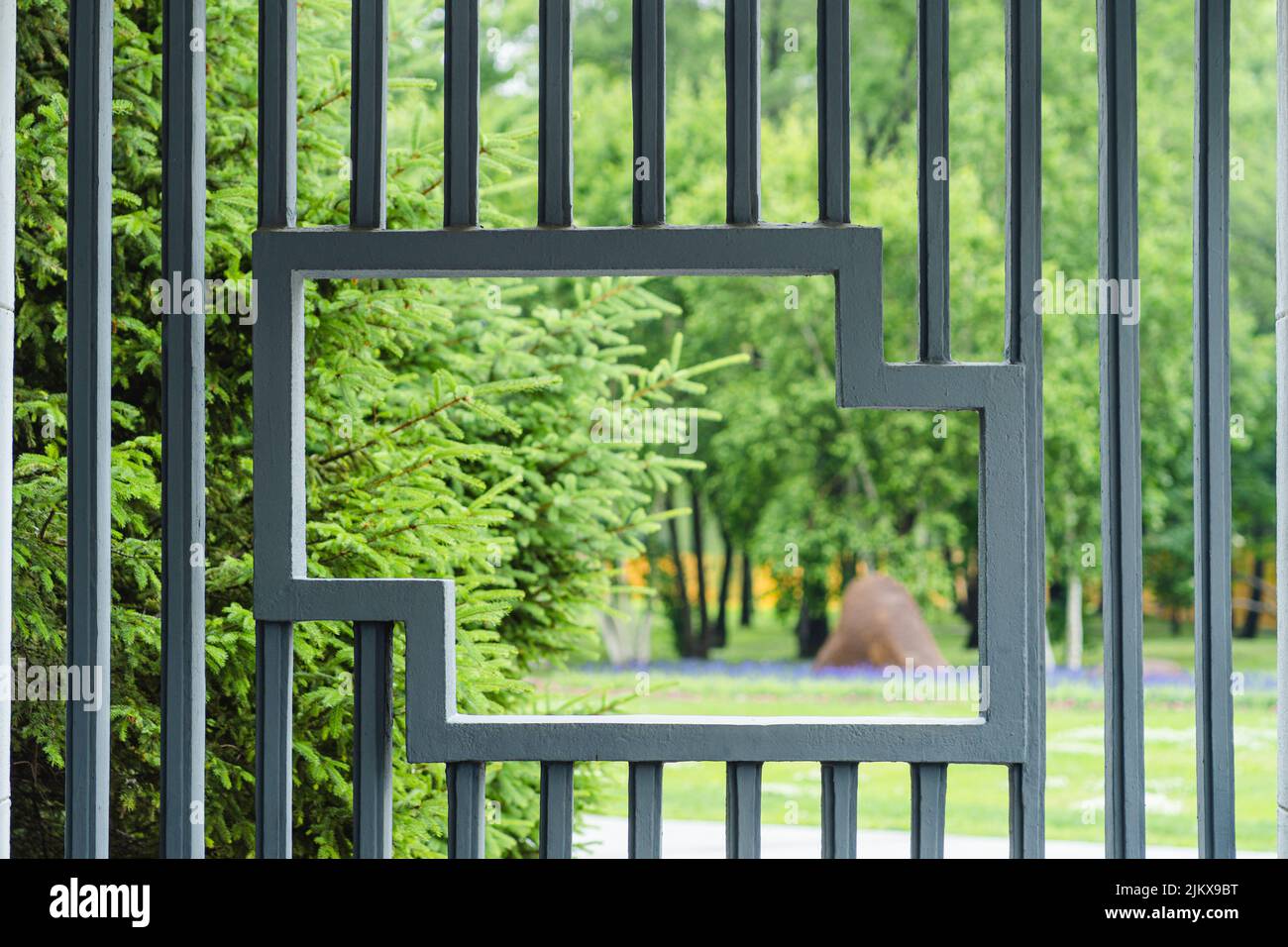 Ein Blick aus einem Loch eines Metallgeländers auf den grünen Park Stockfoto