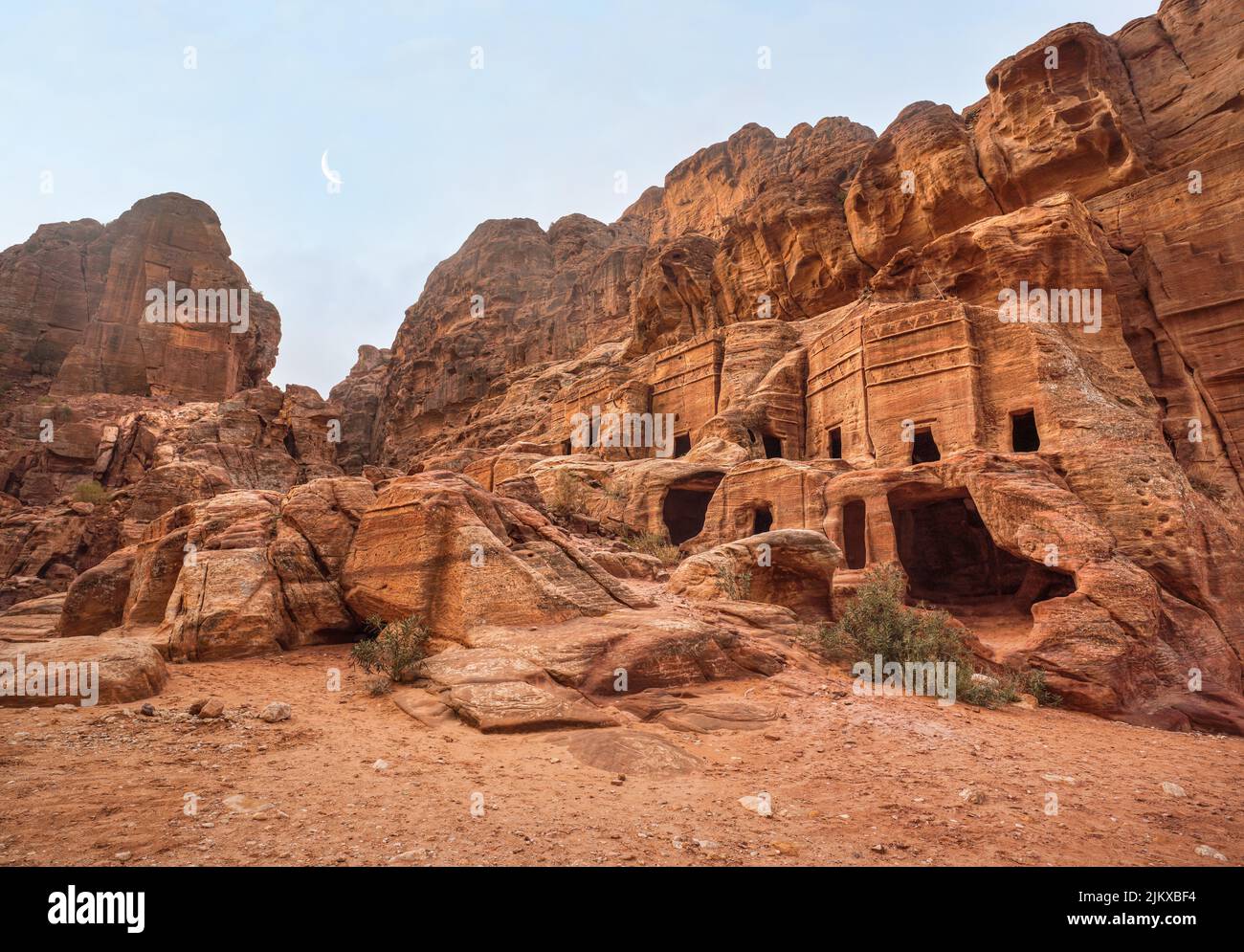 Einfache Wohnruinen - höhlenartige Löcher in Steinmauern, Mond über Bergen - wie in Petra, Jordanien, zu sehen Stockfoto