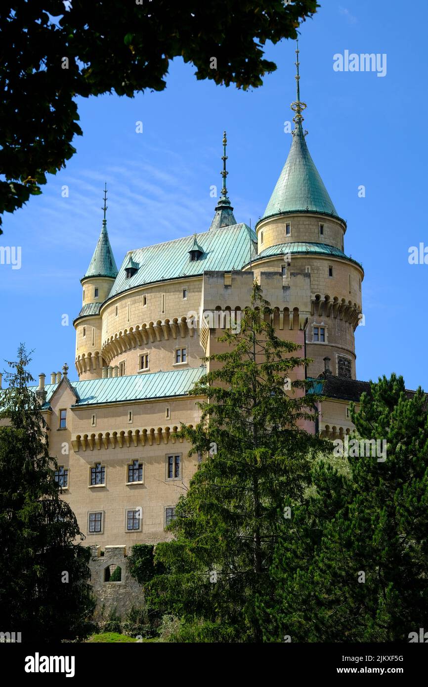 Eine vertikale Aufnahme des historischen Schlosses Bojnice mit blauen Kuppeln in der Slowakei aus dem Rahmen von Bäumen Stockfoto