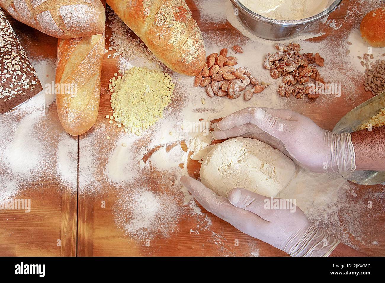 Eine Nahaufnahme der Hände in Handschuhen, die Brot mit Mandeln und Walnüssen backen. Stockfoto