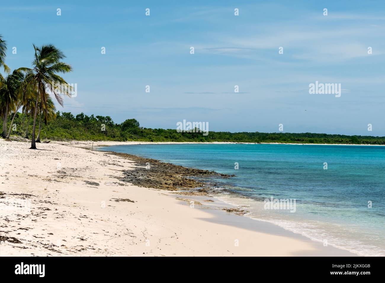 Foto eines kubanischen Strandes mit weißem Sand und etwas Lapiez am Ufer, das Meer ist ruhig und klar, es gibt einige tropische Vegetation in der Ferne Stockfoto