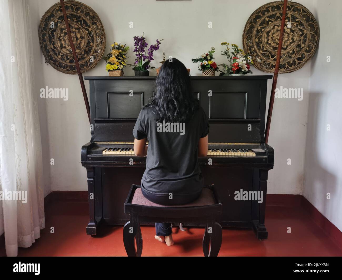 Ein Mädchen in schwarzen Kleidern spielt ein altes schwarzes Klavier Stockfoto