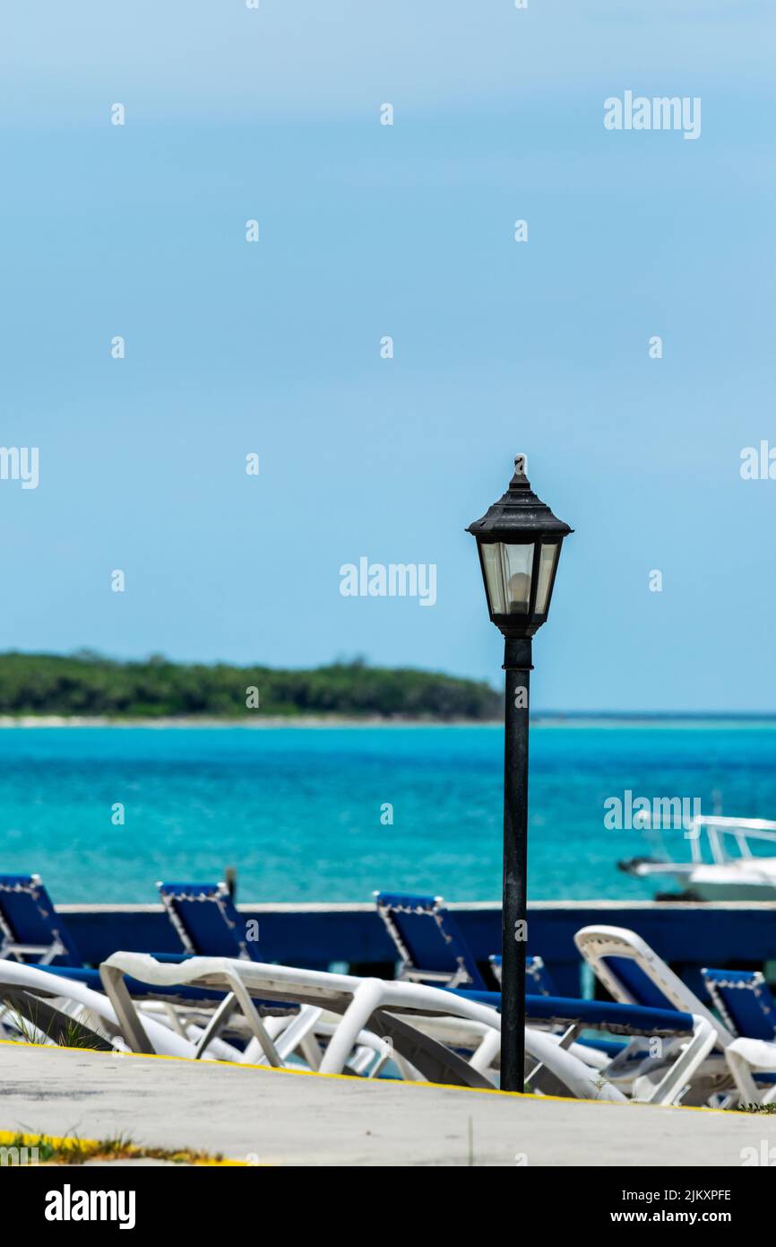 Selektiver Fokus einer einsamen Lampe mit ausgeschaltetem Licht tagsüber an einem karibischen Strand befinden sich im Hintergrund einige Strandliegen, das Meer Stockfoto