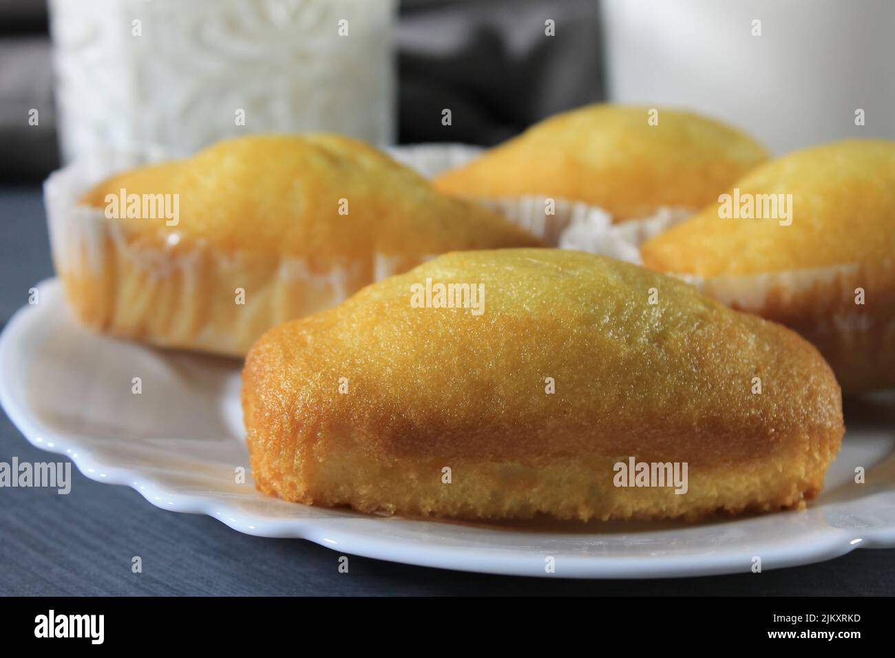Nahaufnahme mehrerer Plumcakes auf einem weißen Teller mit einem Glas Milch daneben auf einem grauen Holztisch Stockfoto
