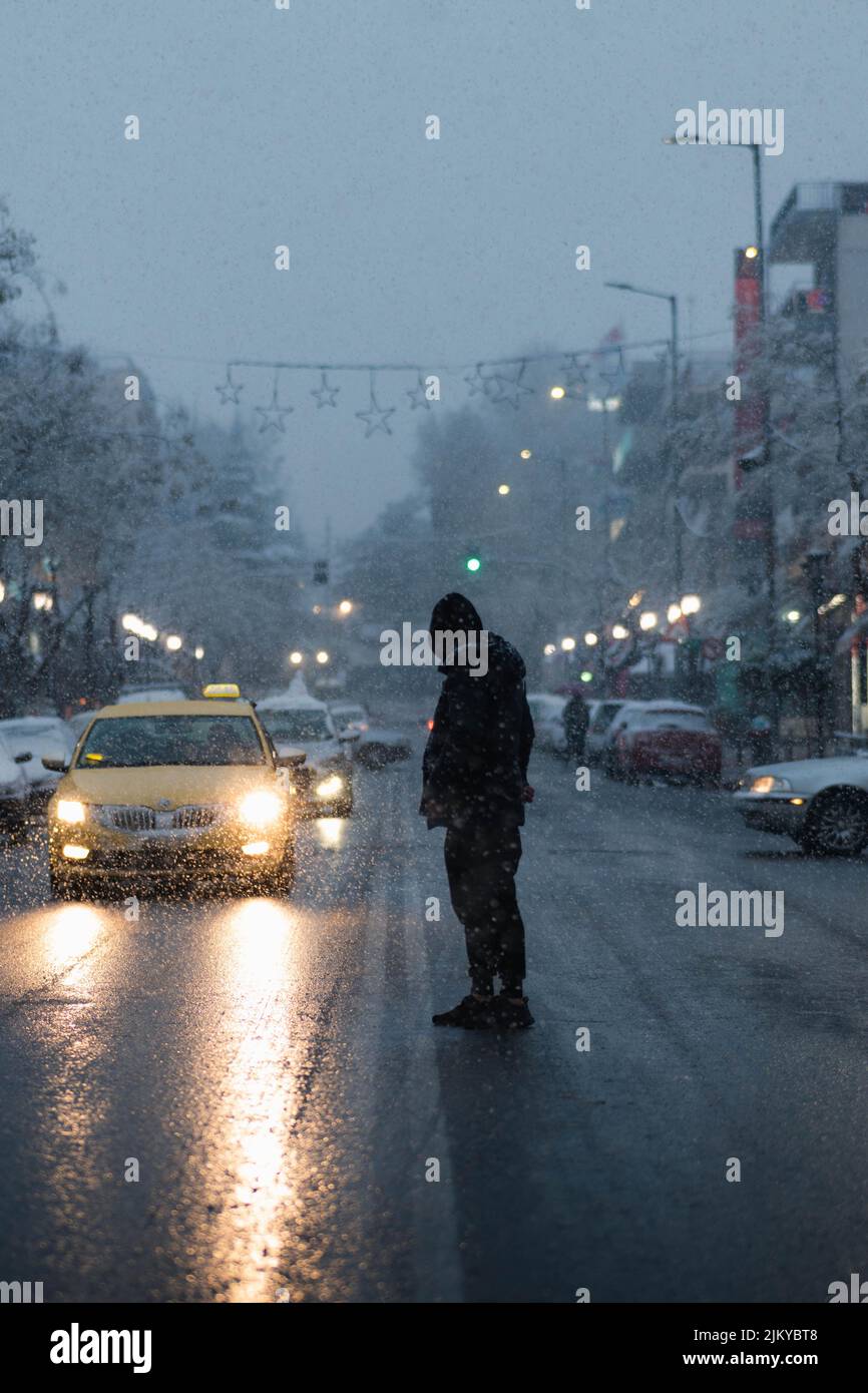 Eine vertikale Aufnahme eines Mannes mit Kapuzenpullover, der bei Regen und kaltem Wetter die Straße überquert Stockfoto