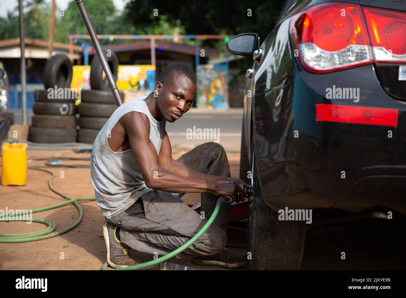 Afrikanischer Mechaniker, der einen Autoreifen mit einem elektronischen Schlagschrauber fixiert, Schuss des Royal Senchi Resort, Akosombo, Ghana an einem sonnigen Tag. Stockfoto