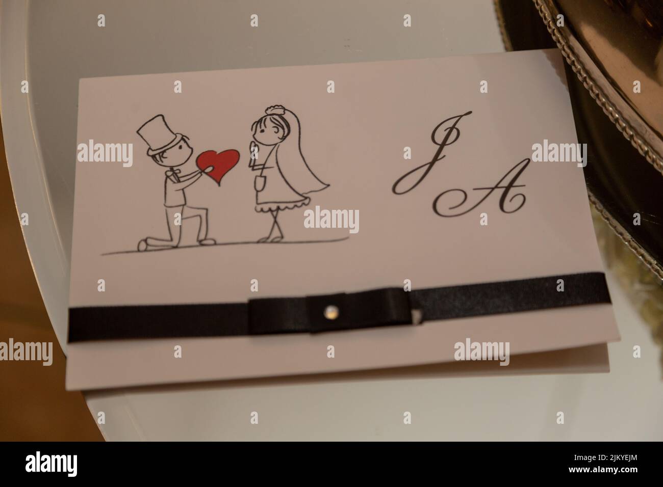 Die Bräutigam-Ikone, die einer Braut ein Herz gibt, mit Buchstaben J und Einem Design einer Hochzeitseinladung Stockfoto