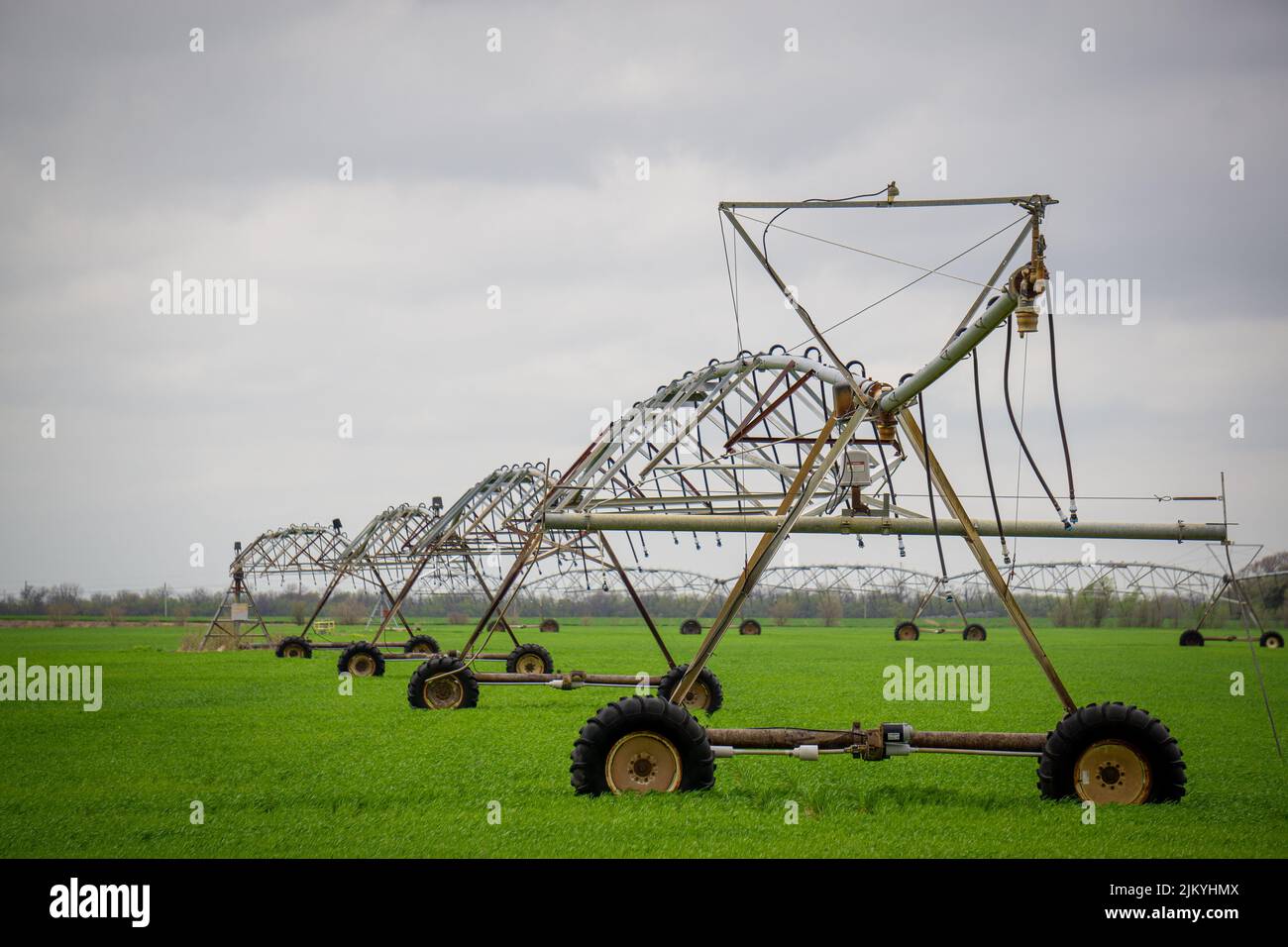 Eine große Anzahl von Bewässerungssystemen auf einem großen grünen Feld mit einem bewölkten Himmel Stockfoto
