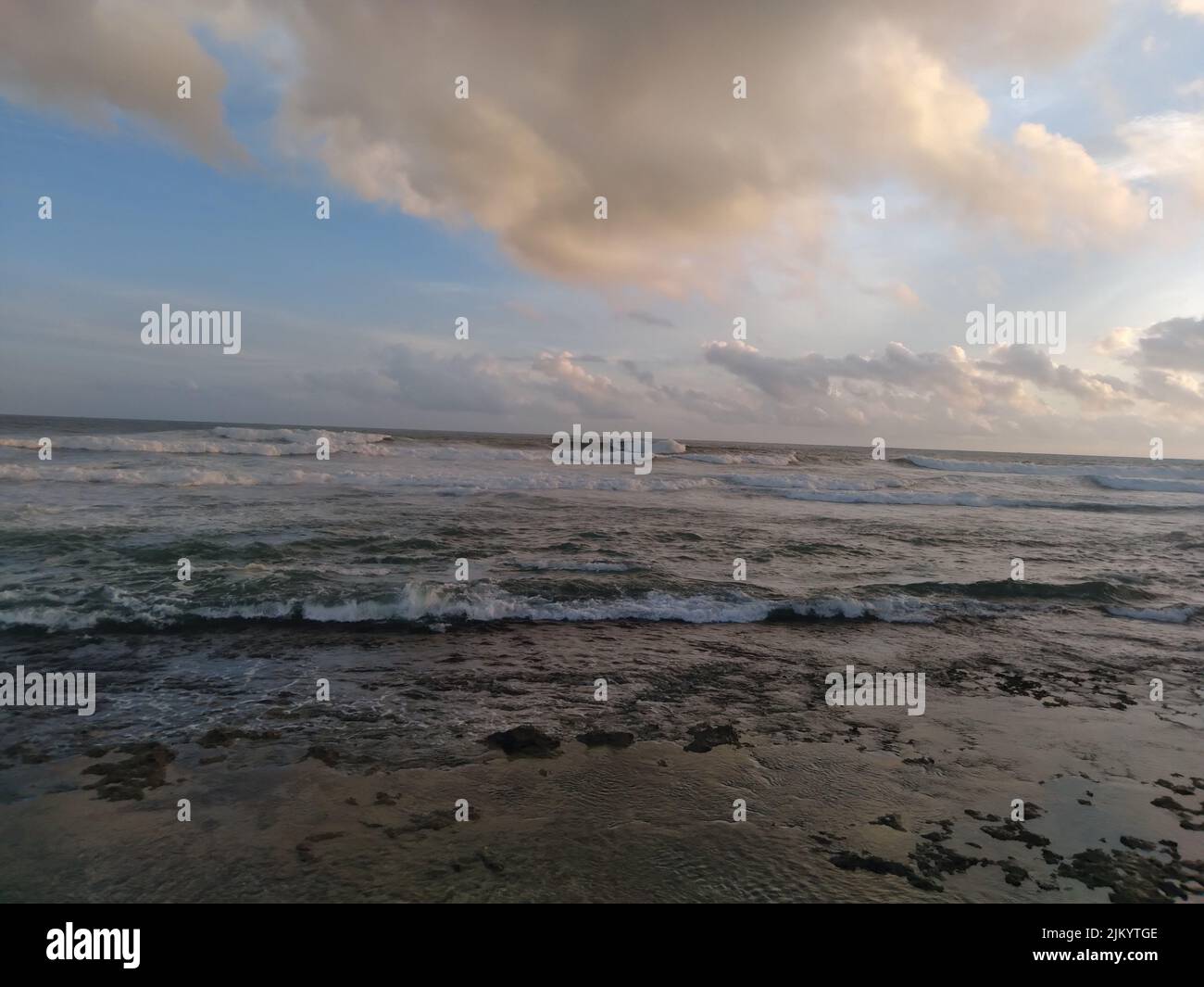 Ein malerischer Blick auf den Strand und das Meer gegen den blau bewölkten Himmel bei Sonnenaufgang Stockfoto