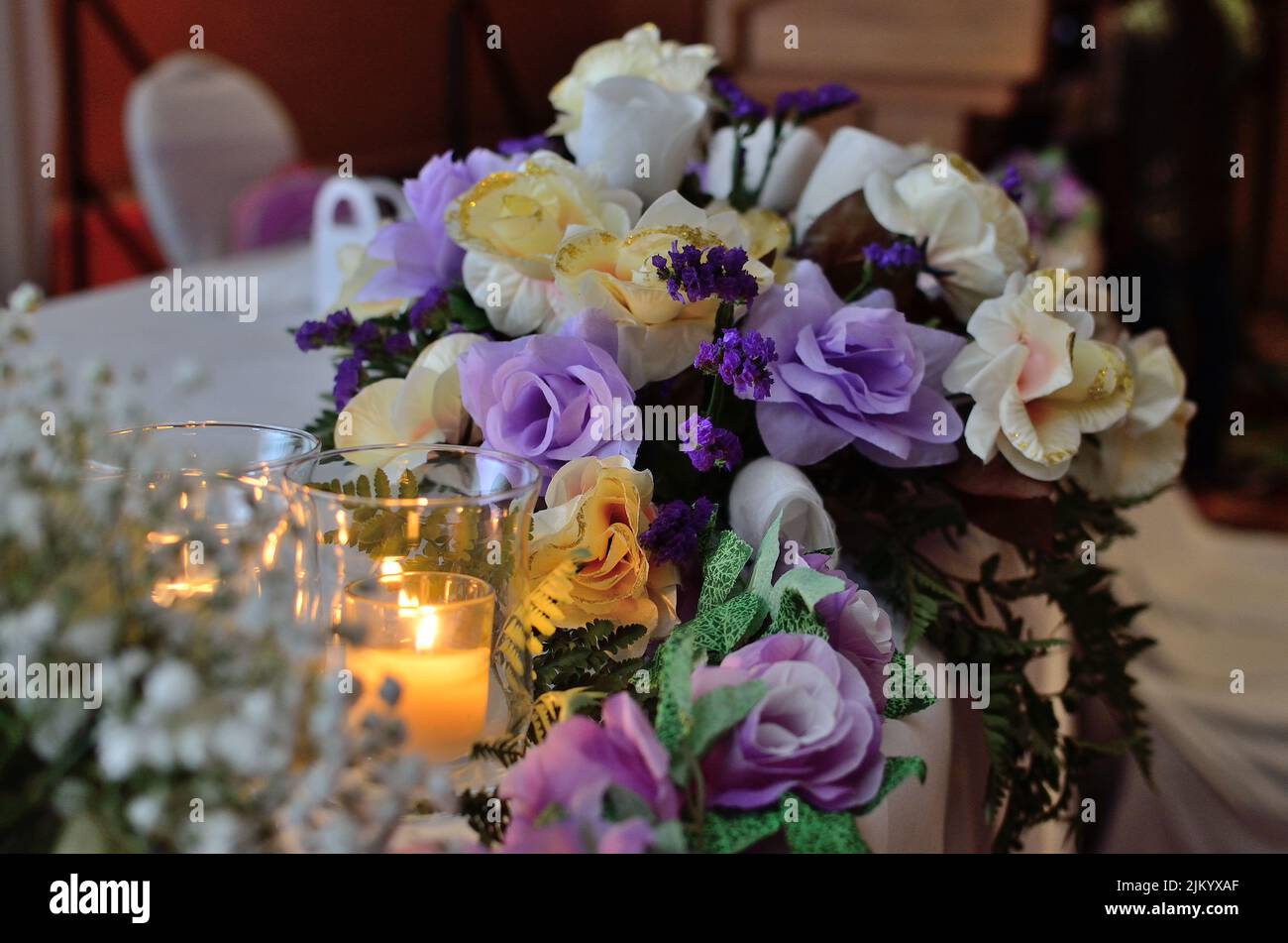 Ein schönes dekoratives Blumenarrangement neben brennenden Kerzen auf einem Tisch Stockfoto