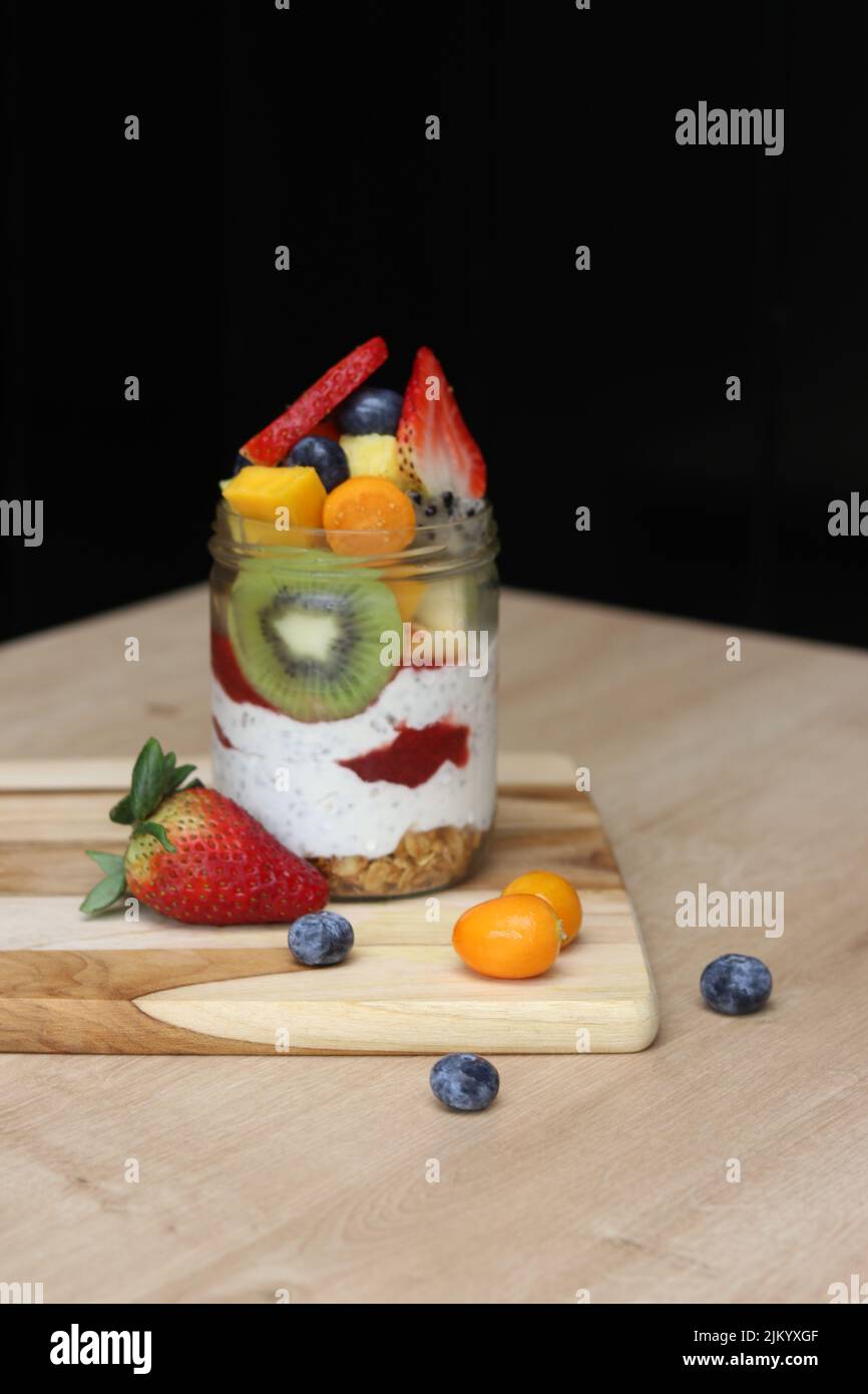 Ein köstlicher Chia-Parfait mit verschiedenen Früchten in einem Glas auf einem Holzbrett auf einem Tisch Stockfoto
