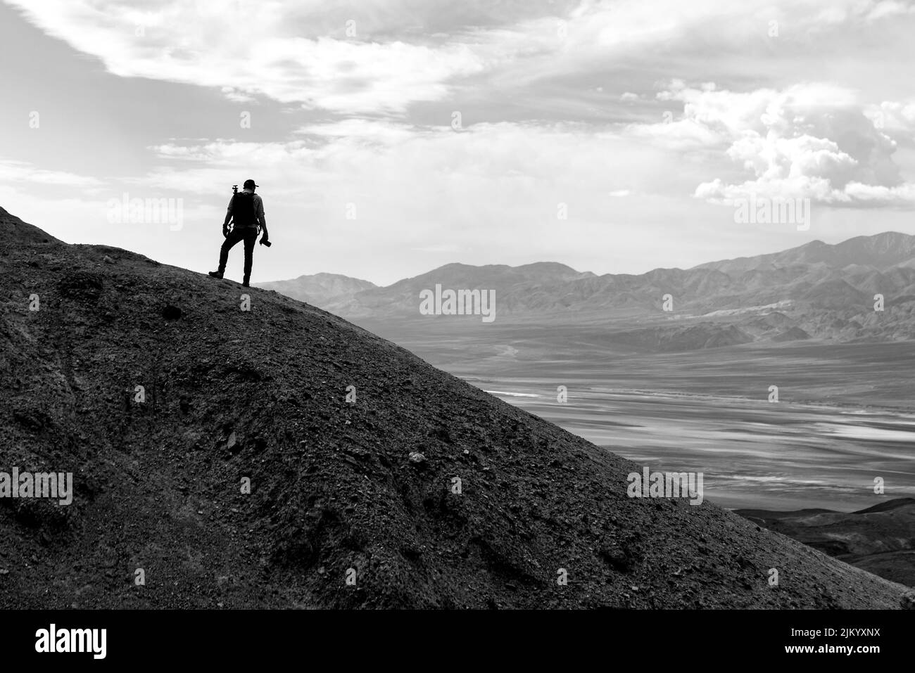 Eine Graustufenaufnahme eines Mannes, der auf einem Hügel steht und die Natur bewundert Stockfoto