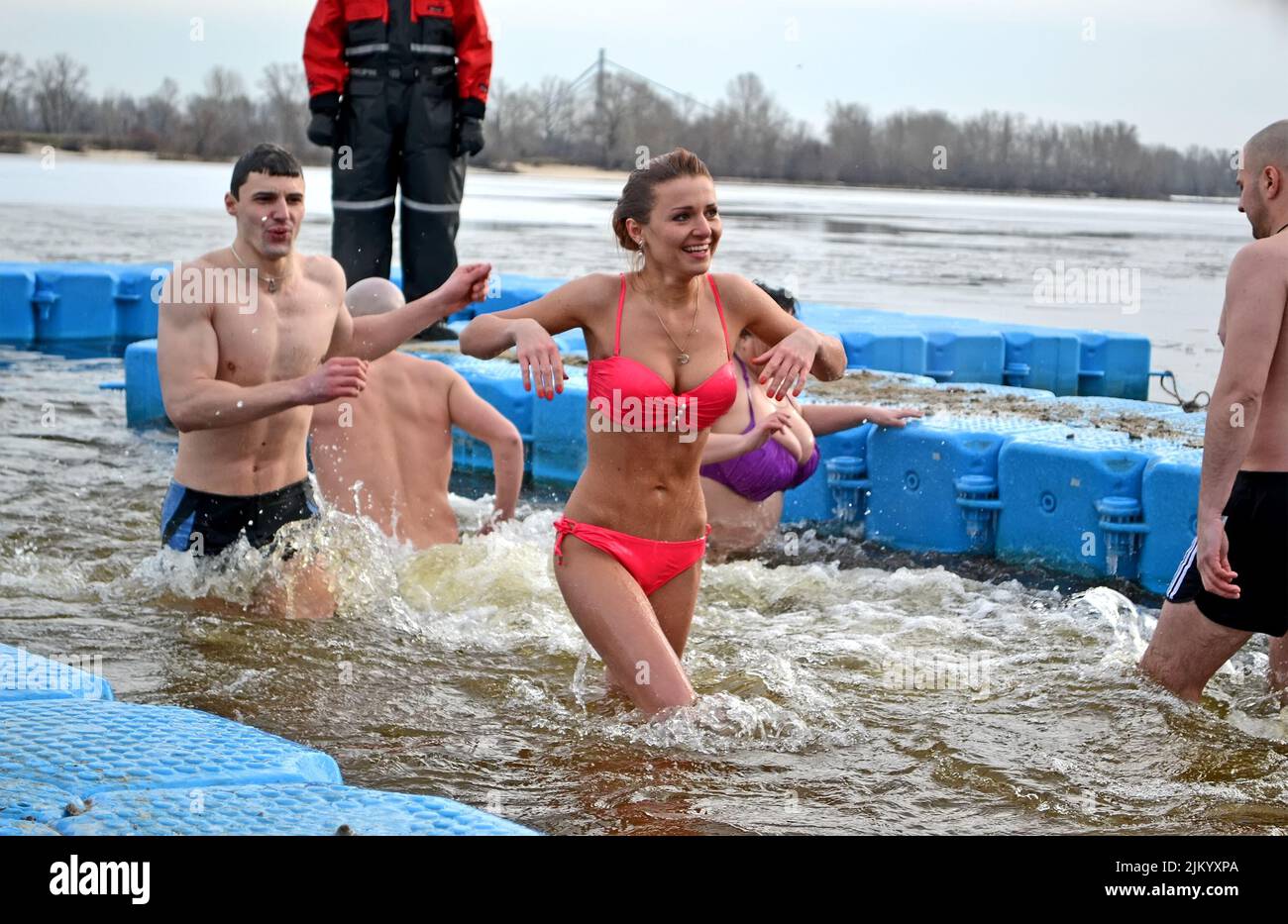 Junge Frau lächelt in rotem BH im kalten Wasser. Epiphany in Kiew, Ukraine. Menschen, die in eiskaltes Wasser tauchen.Es hilft dem Körper, resistent gegen Viren zu werden. Stockfoto