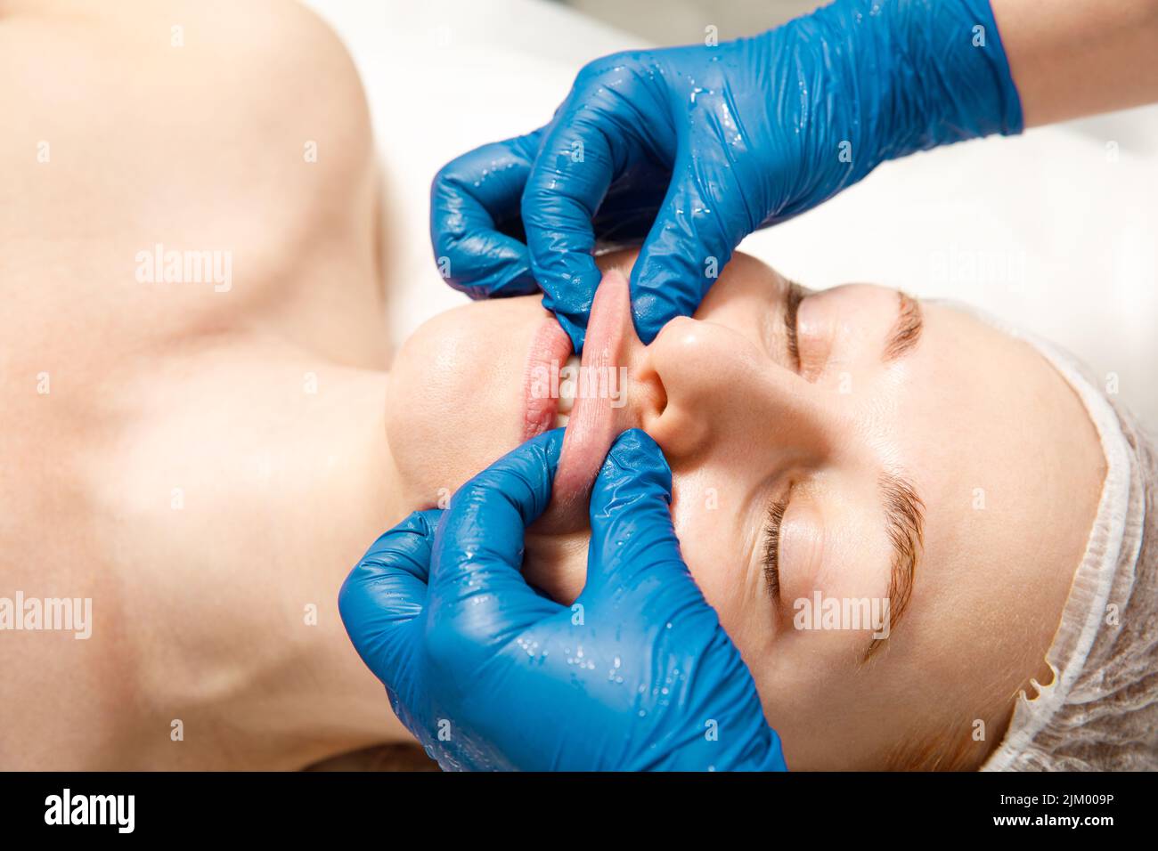 Eine verjüngende Behandlung für die Gesichtshaut. Der Kosmetologe macht eine bukkale Massage der Gesichtsmuskeln des Patienten. Stockfoto