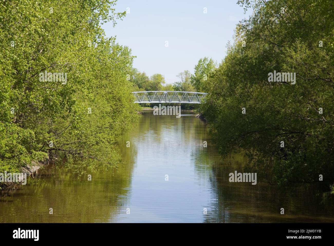 Fußgängerbrücke über den Fluss, im Frühjahr mit Laubbäumen gesäumt. Stockfoto