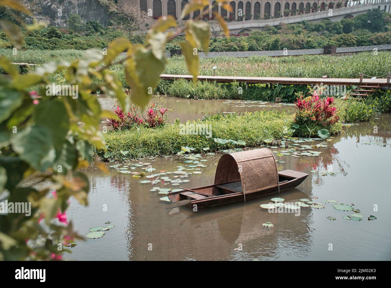 Ein kleines Boot in einem Teich mit Pflanzen, Blumen und Gras Stockfoto