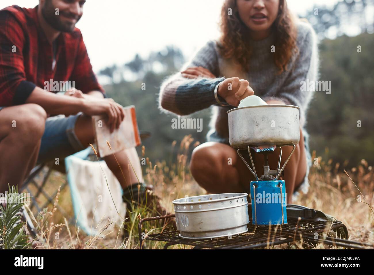 Junge Frau, die mit ihrem Freund zusammen auf einem Gasherd Essen zubereitete. Abenteuerliches junges Paar, das im Wald zeltet. Stockfoto