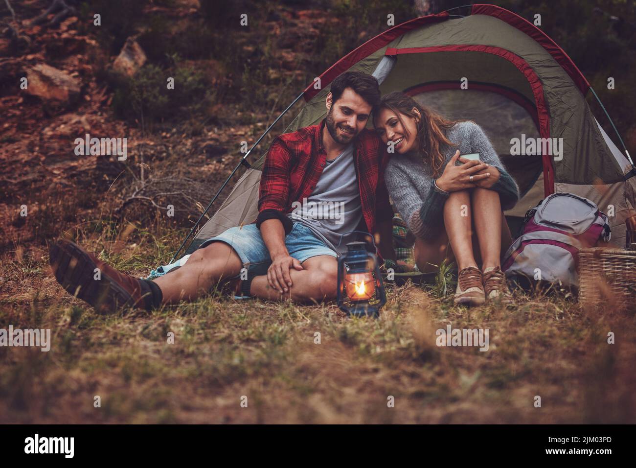 Glückliches junges Paar, das am Abend in der Nähe eines Campingzelts sitzt. Junges Paar genießt einen Campingurlaub zusammen. Stockfoto
