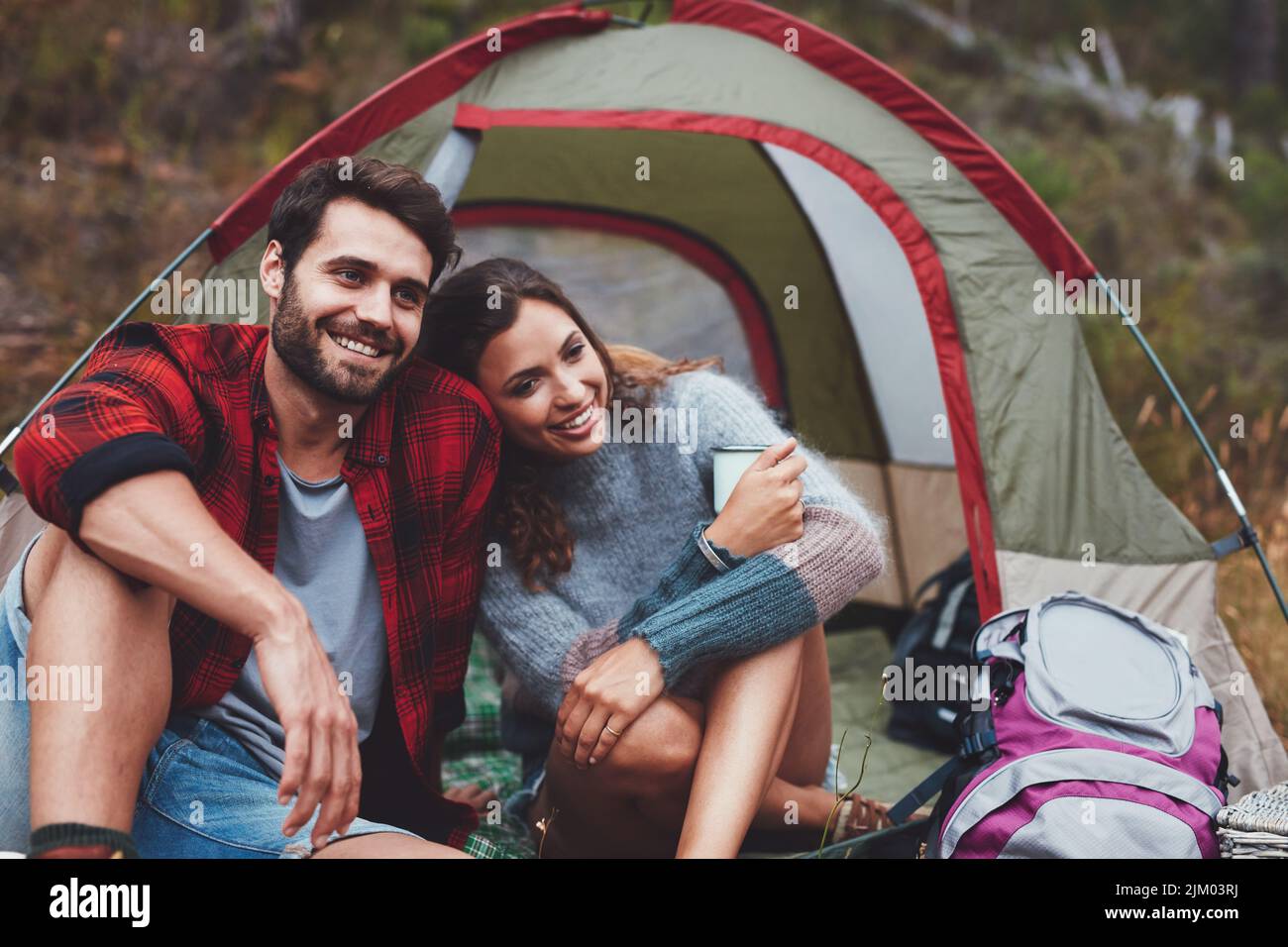 Liebevolles Paar lächelt fröhlich, während es vor dem Zelt sitzt. Junges Paar, das sich entspannt und eine gute Zeit zusammen auf einem Campingurlaub verbringt. Stockfoto