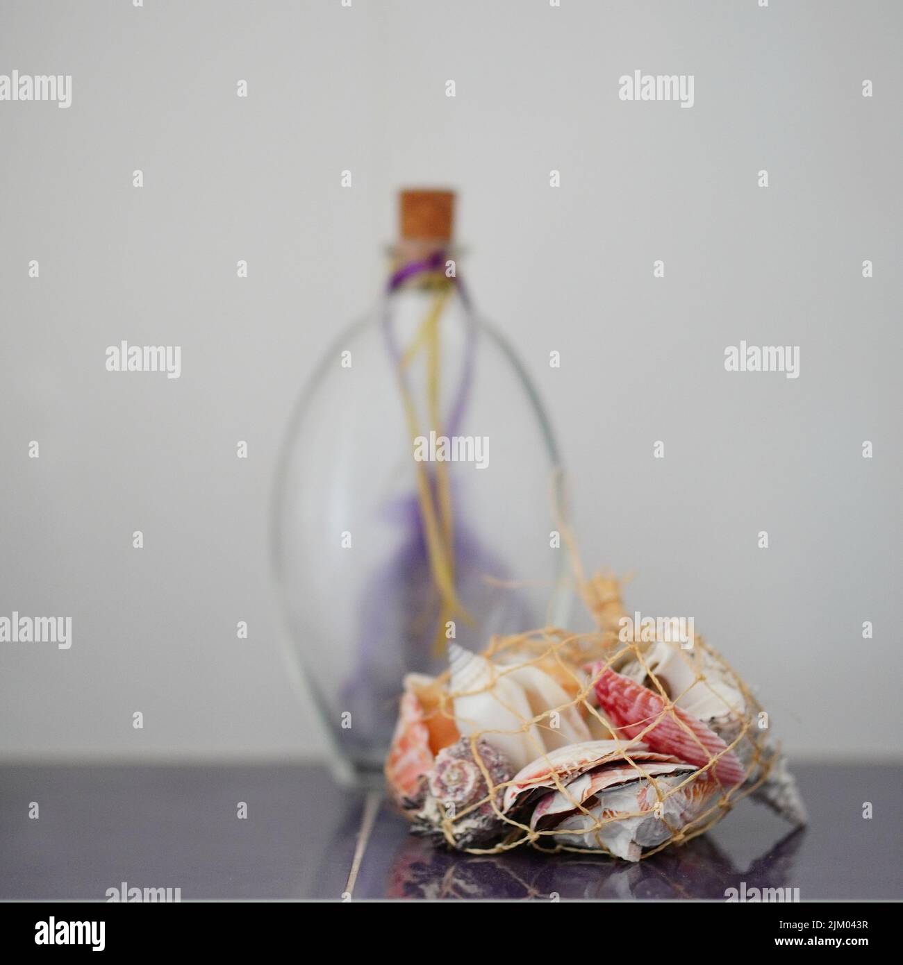 Eine vertikale selektive Fokusaufnahme von Muscheln in einem kleinen Netz auf einem unscharfen Hintergrund einer Glasflasche Stockfoto