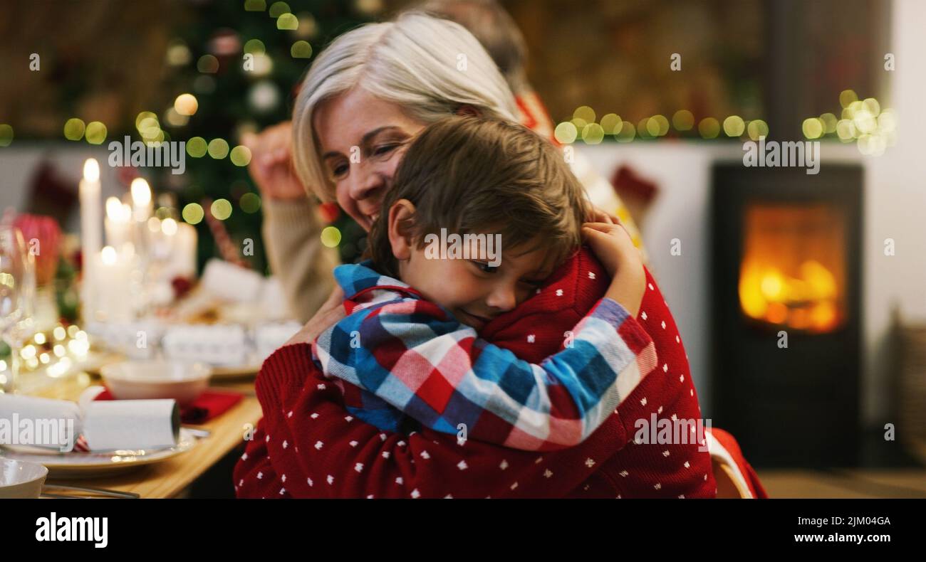 Mein Lieblingsweihnachtsgeschenk nennt mich Oma. Eine liebevolle ältere Frau umarmte ihren Enkel während einer Weihnachts-Dinner-Party zu Hause. Stockfoto