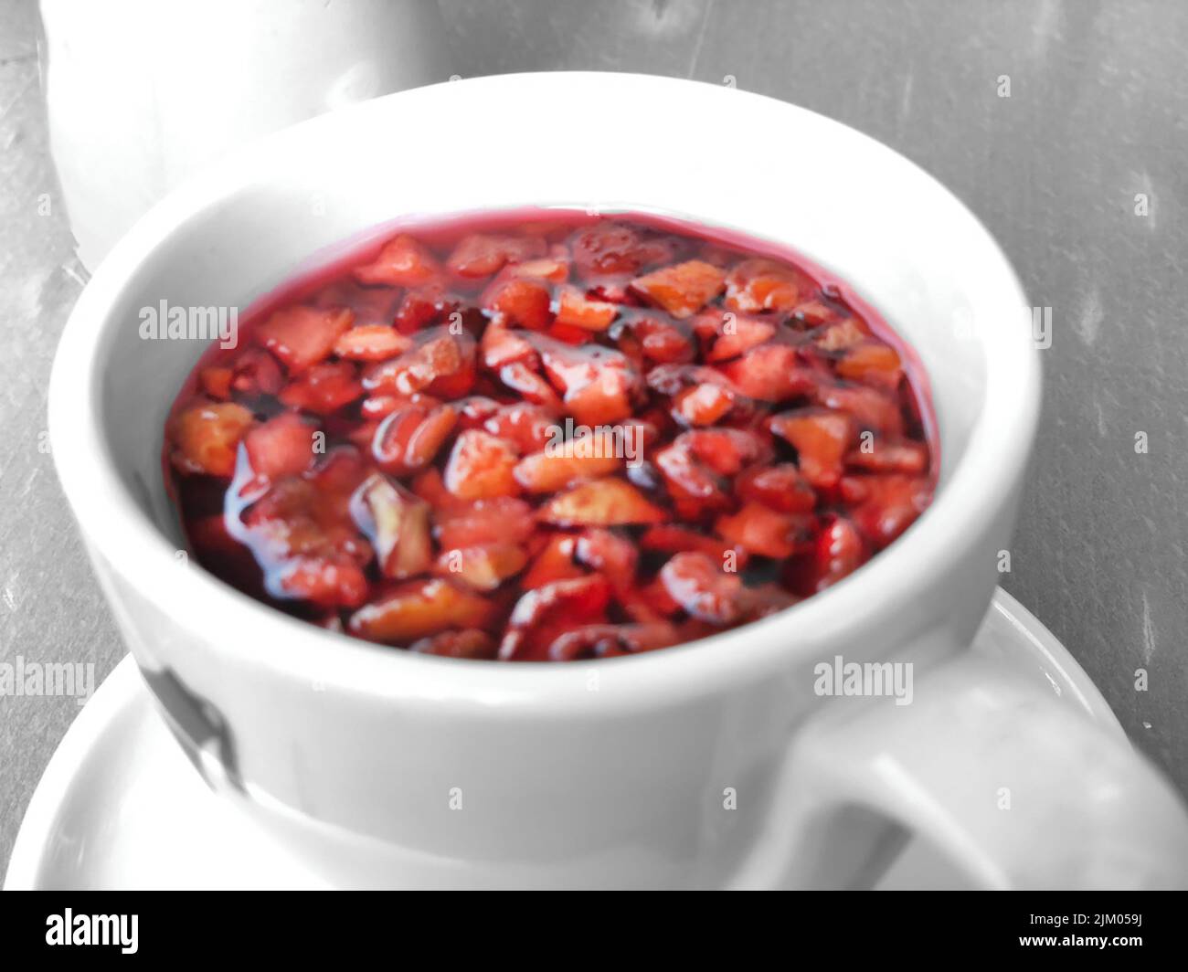 Roter Früchtetee in weißer Tasse mit Fruchtstücken darin. Stockfoto