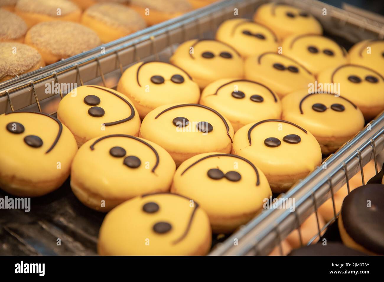 Eine Nahaufnahme von süßen Donuts mit gelb lächelnden Gesichtern auf dem Regal in einer Konditorei Stockfoto