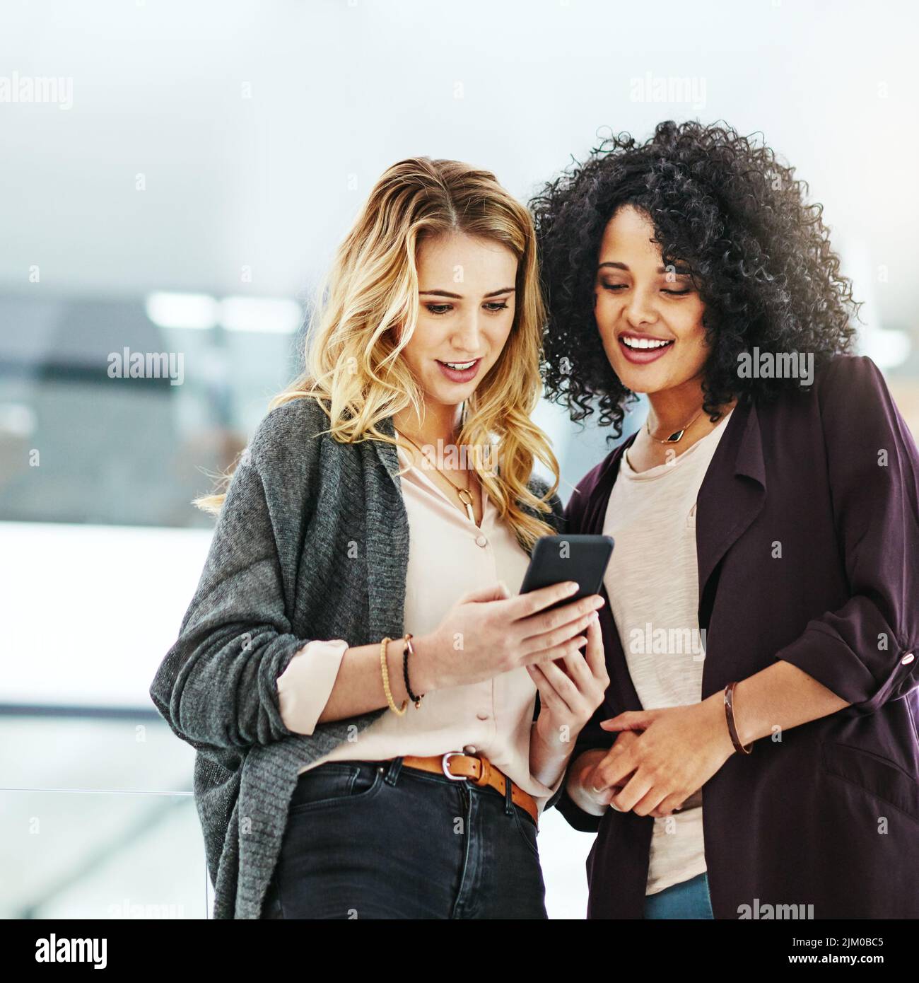 Geschäftsfrauen, die bei der Arbeit in ihrem Büro am Telefon surfen. Eine Kollegin zeigt ihrem Kollegen auf einem Handy bei der Arbeit ein Design, eine Idee oder einen Plan Stockfoto