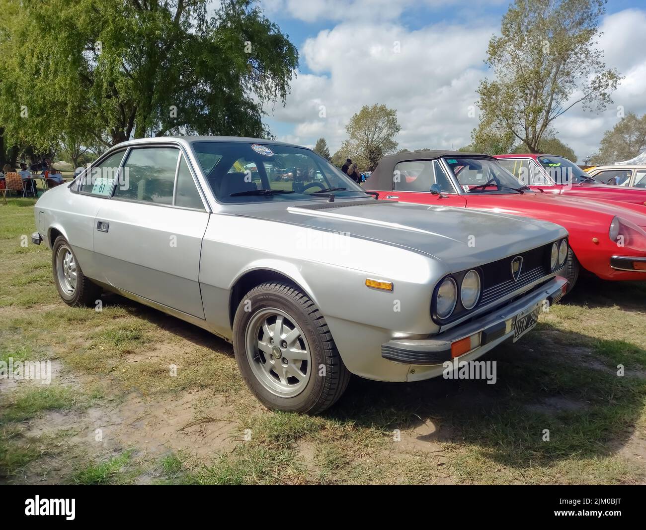 Chascomus, Argentinien - 9. Apr 2022: Altes grausilbernes Lancia Beta Coupé Ende 1970s auf dem Rasen geparkt. Naturbäume im Hintergrund. Oldtimer-Show Stockfoto