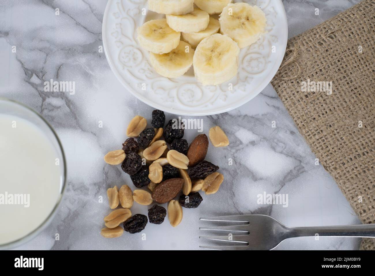 Ein Blick von oben auf einen Wandermix auf einem weißen Teller mit geschnittenen Bananen und Milch auf einem Marmortisch Stockfoto