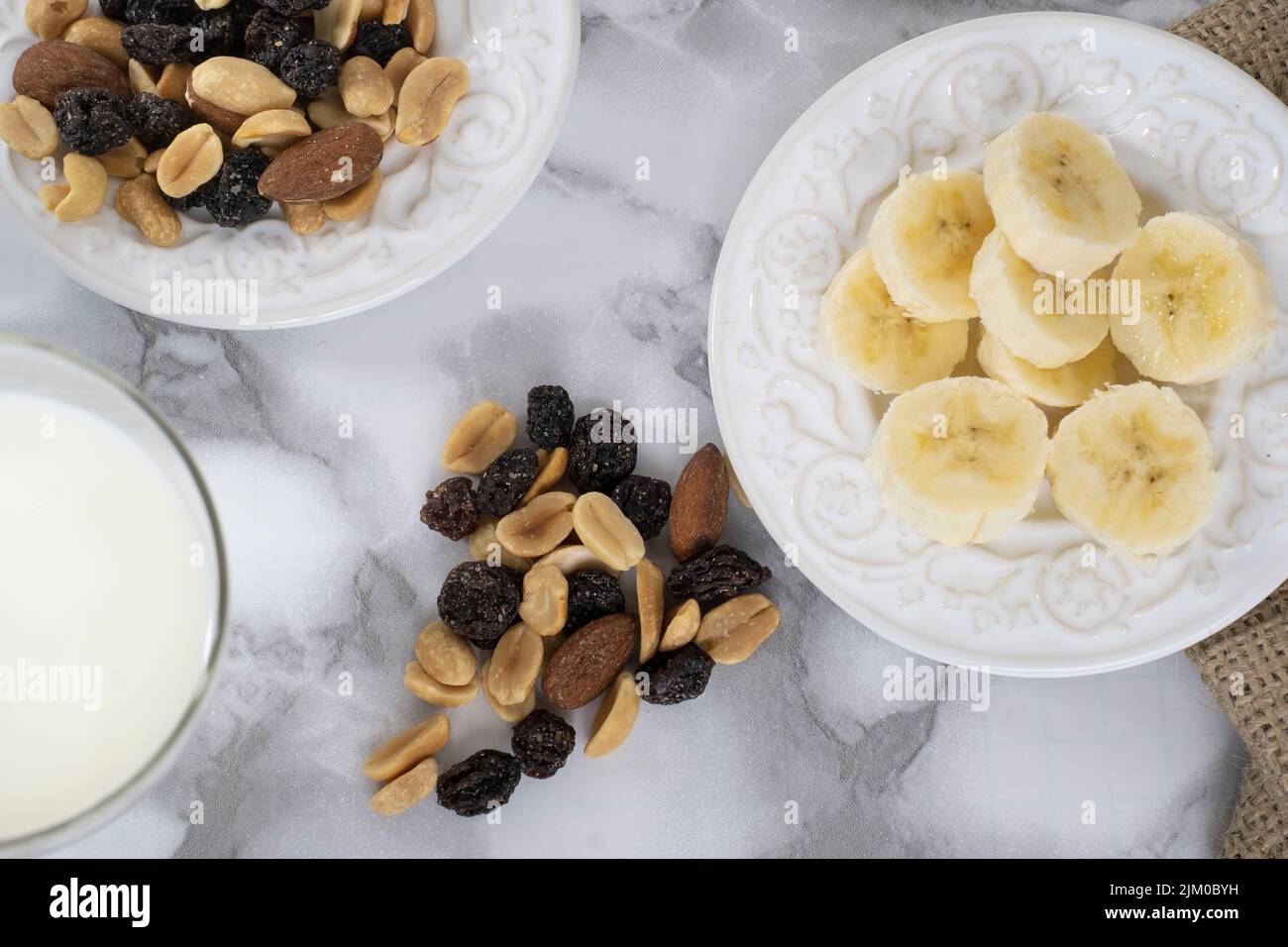 Ein Blick von oben auf einen Wandermix auf einem weißen Teller mit geschnittenen Bananen und Milch auf einem Marmortisch Stockfoto