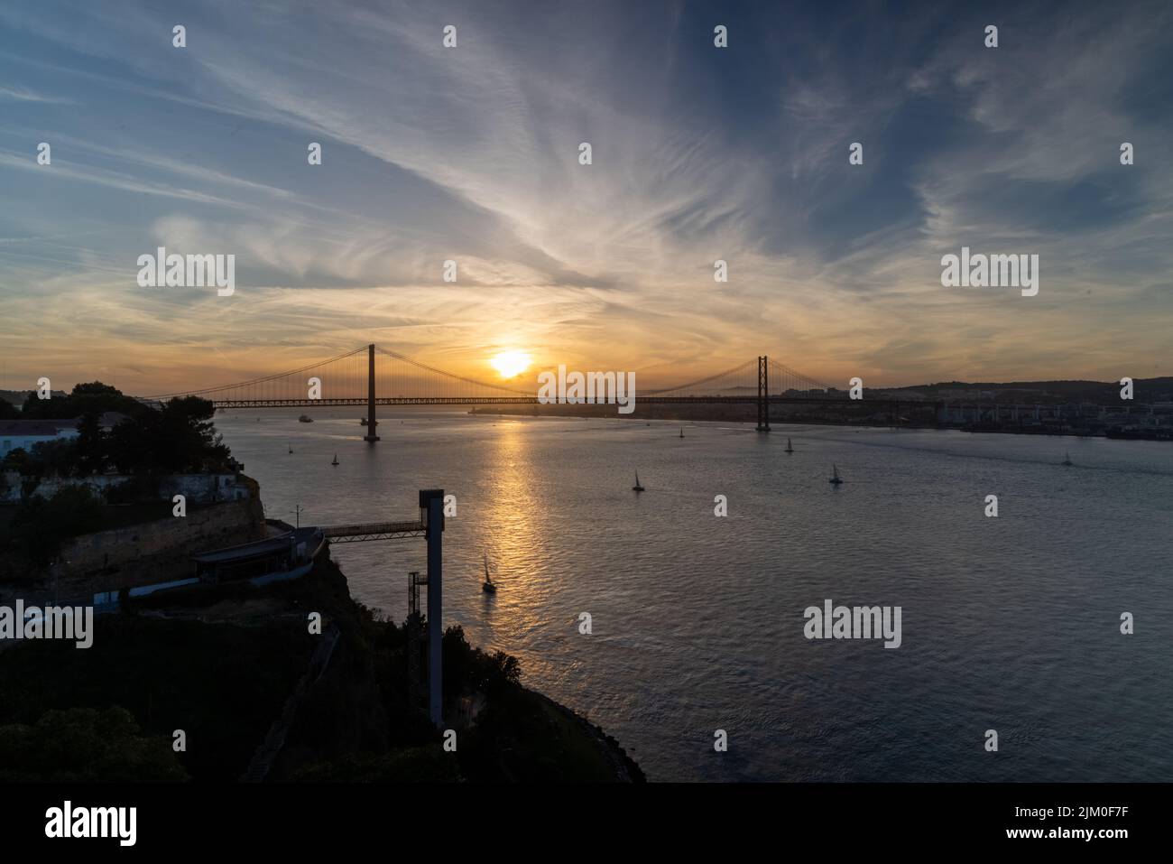 Ein schöner Blick auf die Brücke über den Fluss in Lissabon, Portugal bei orangefarbenem Sonnenuntergang Stockfoto