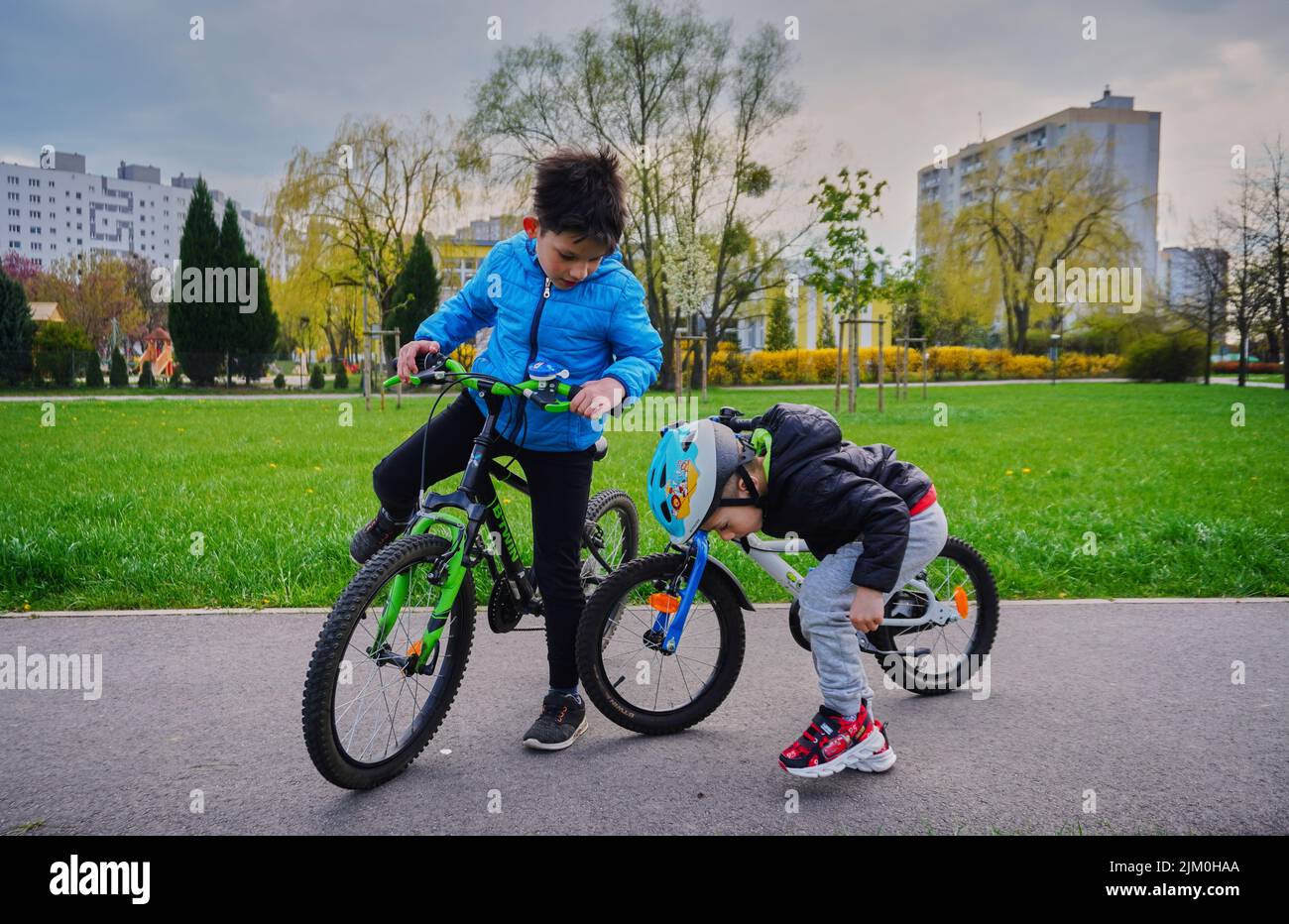 Ein kleiner Junge auf einem Fahrrad und ein anderer auf einem Asphaltweg auf der Suche nach etwas in einem Park im Bezirk Orla Bialego. Stockfoto