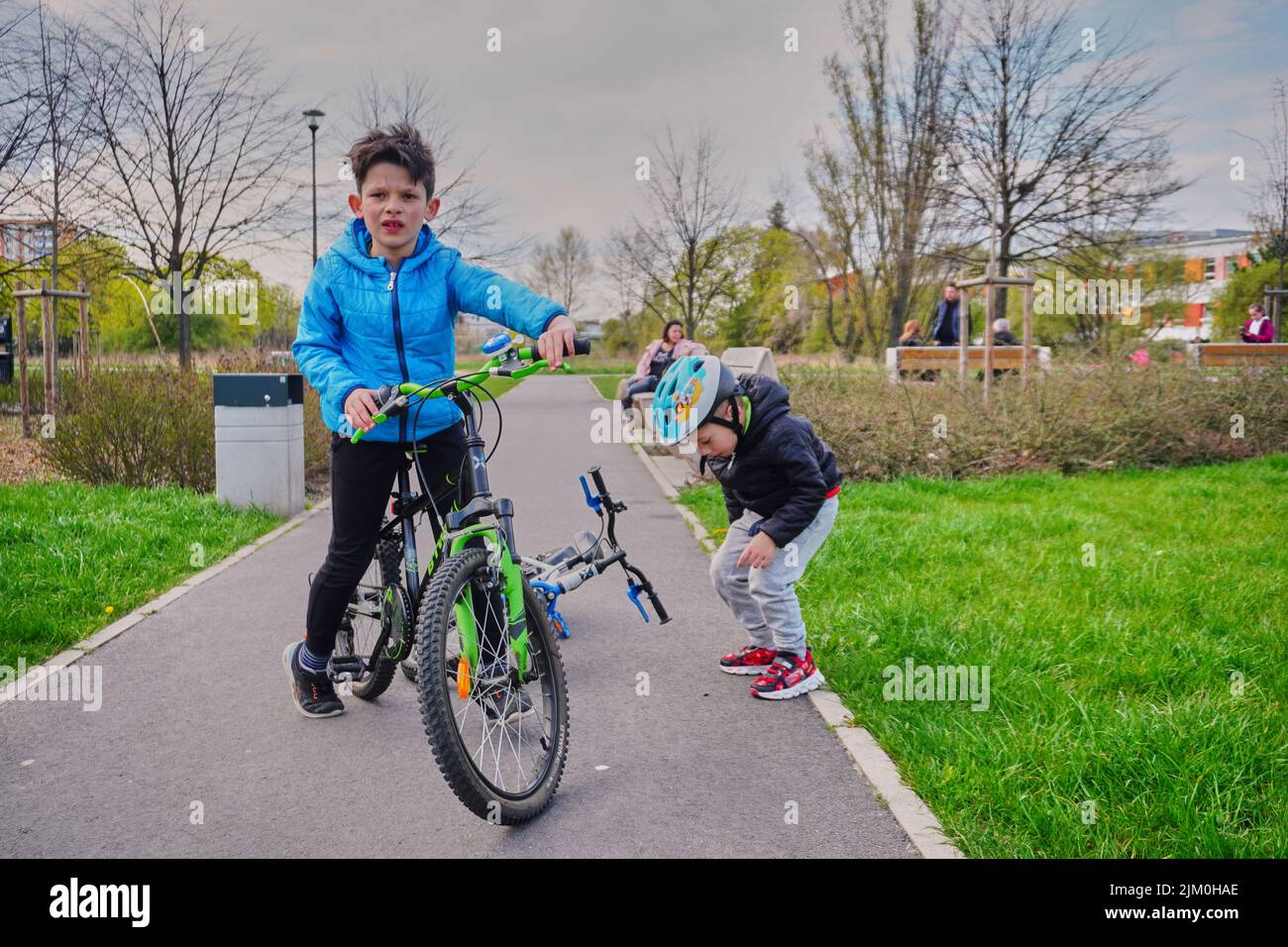 Ein kleiner Junge auf einem Fahrrad und ein anderer auf einem Asphaltweg auf der Suche nach etwas in einem Park im Bezirk Orla Bialego Stockfoto