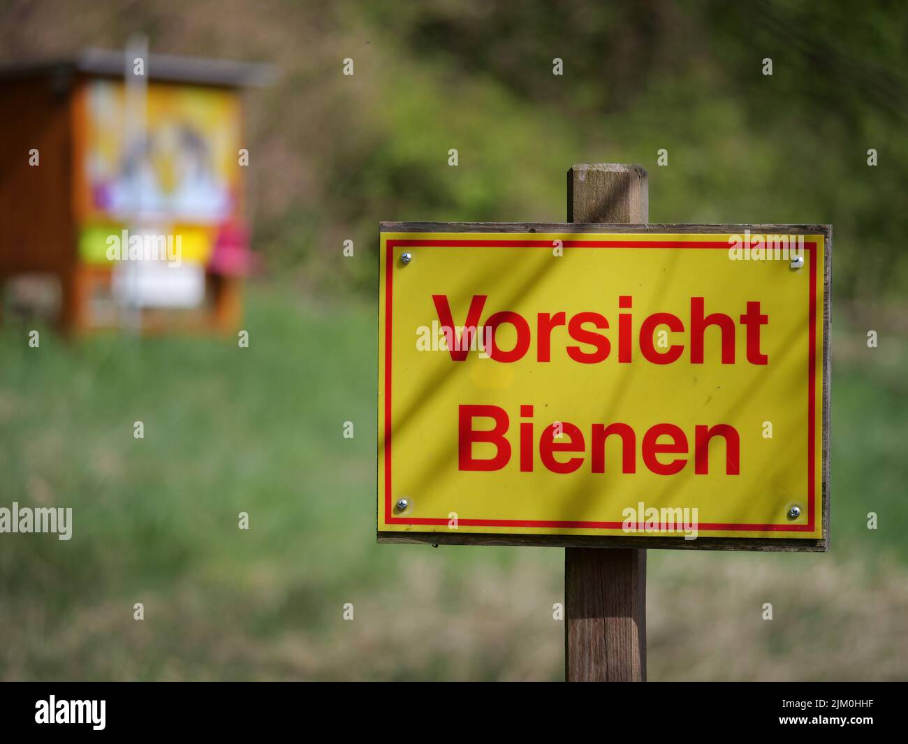 Ein Schild, das vor einem Bienenstock auf einer Wiese warnt Stockfoto
